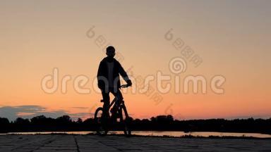 少年骑自行<strong>车</strong>沿着河堤前行.. 体育生活方式。 骑自行<strong>车</strong>的<strong>剪影</strong>。